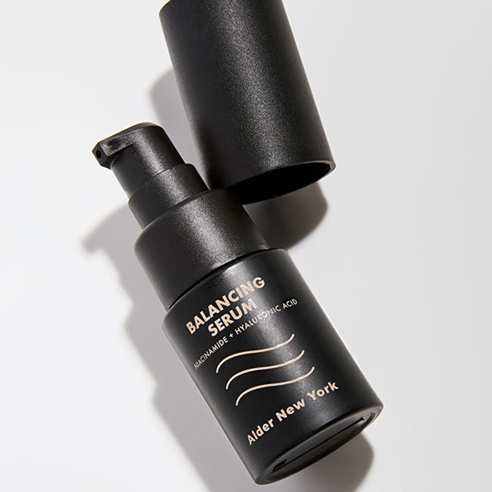 Black bottle of Alder New York Balancing Serum on a white surface with cap next to it