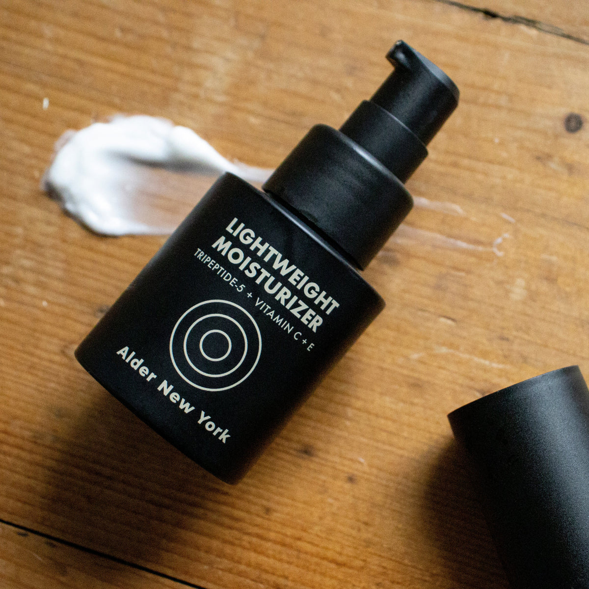 Alder New York's Lightweight Moisturizer bottle on a wood surface with a swipe of cream