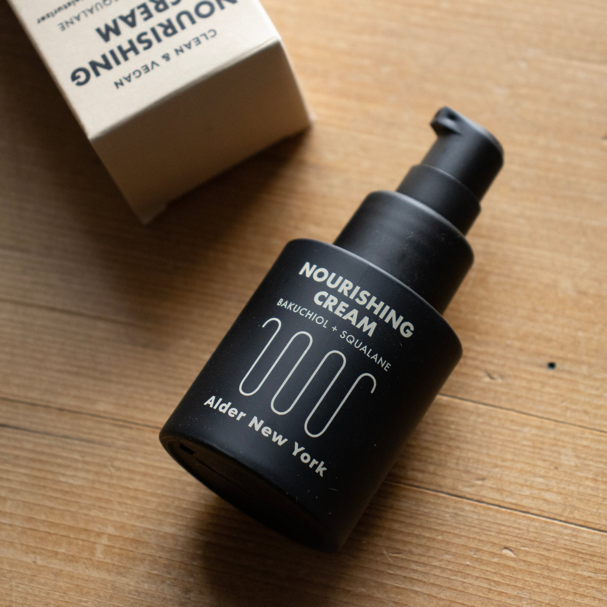 A Bottle of Alder New York Nourishing Cream on a wood surface